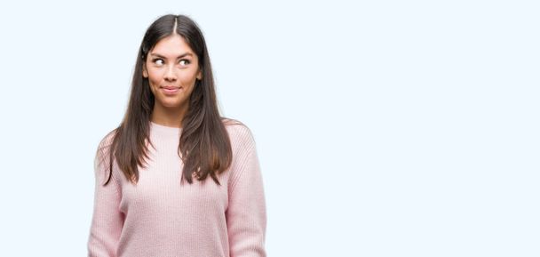 Joven mujer hispana hermosa usando un suéter sonriendo mirando lado y mirando hacia otro lado pensando
. - Foto, imagen