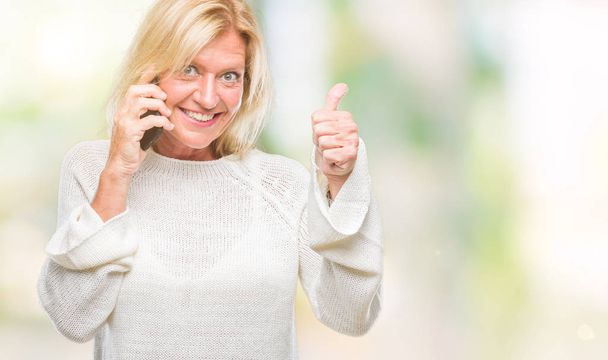 Middle age blonde woman talking on smartphone over isolated background happy with big smile doing ok sign, thumb up with fingers, excellent sign - Φωτογραφία, εικόνα
