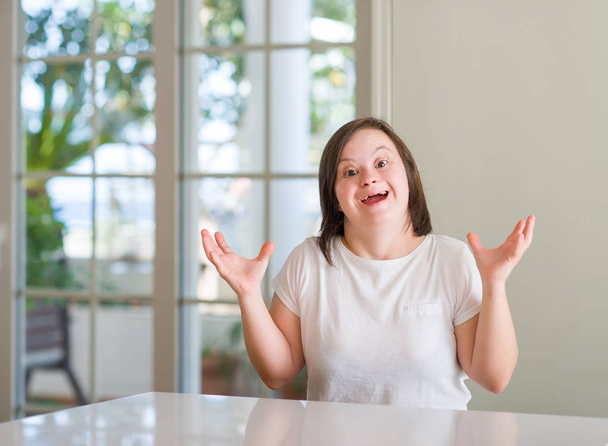 Down-Syndrom-Frau zu Hause sehr glücklich und aufgeregt, Siegerausdruck feiert Sieg schreiend mit breitem Lächeln und erhobenen Händen - Foto, Bild