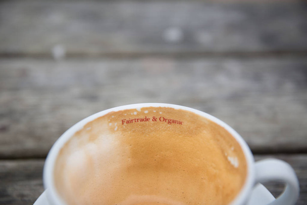 Close up da superfície de uma xícara de café cappuccino com uma bebida quente cremosa dentro com um sinal informando comércio justo e grãos de café orgânicos foram fornecidos e fornecidos para esta bebida
 - Foto, Imagem