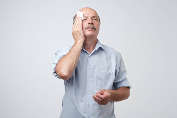 Tired old man with mustache stressed sweating having fever headache isolated on gray wall background - Photo, Image