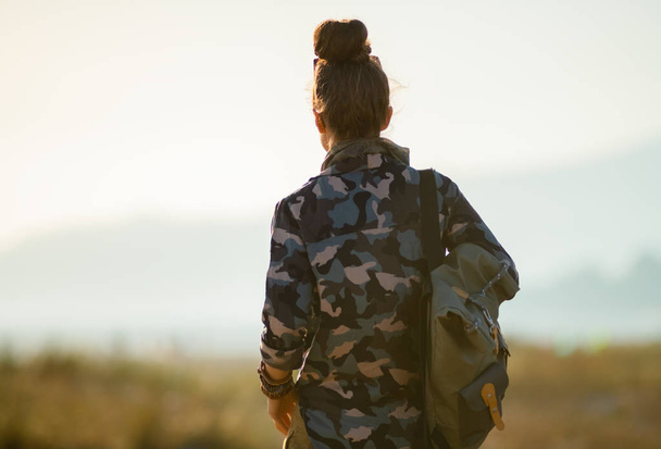 back view of tourist woman in hiking gear against mountain and ocean landscape at sunset - Fotografie, Obrázek