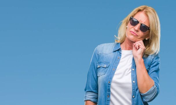 Middle age blonde woman wearing sunglasses over isolated background with hand on chin thinking about question, pensive expression. Smiling with thoughtful face. Doubt concept. - Photo, Image