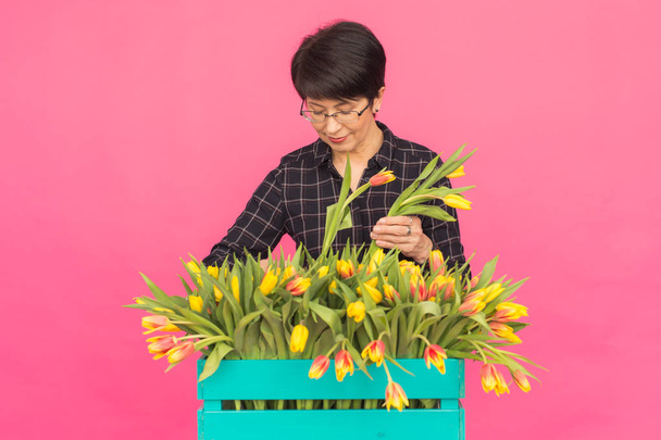 Middle-aged caucasian woman with box of tulips in pink studio. - Photo, Image