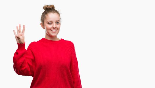 Młoda kobieta blonde noszenie bun i czerwony sweterek pokazując i skierowaną w górę palcami numer cztery jednocześnie uśmiechając się pewnie i wygodnie. - Zdjęcie, obraz