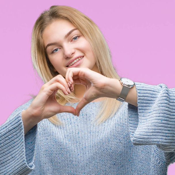 Young caucasian woman wearing winter sweater over isolated background smiling in love showing heart symbol and shape with hands. Romantic concept. - 写真・画像