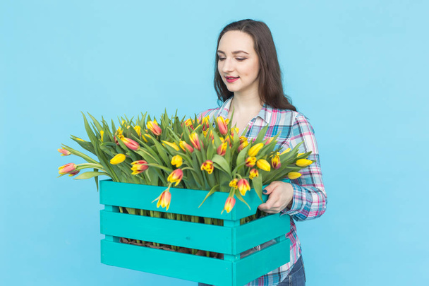 Prachtige vrouwelijke tuinman holding doos met tulpen op blauwe achtergrond - Foto, afbeelding