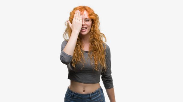 Young redhead woman covering one eye with hand with confident smile on face and surprise emotion. - Photo, Image