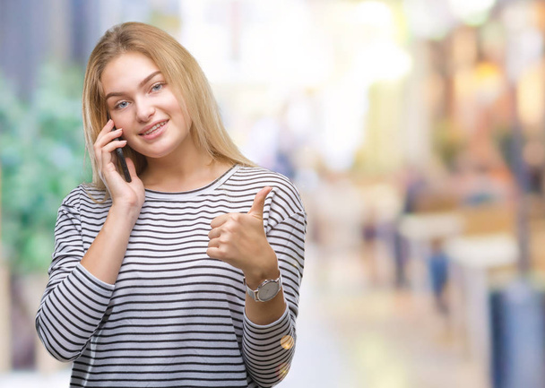 Mulher branca jovem mostrando tela do smartphone sobre fundo isolado feliz com grande sorriso fazendo sinal ok, polegar com os dedos, excelente sinal
 - Foto, Imagem