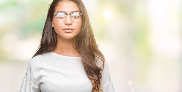 Jovem bela mulher árabe vestindo óculos sobre fundo isolado com expressão séria no rosto. Simples e natural olhando para a câmera
. - Foto, Imagem