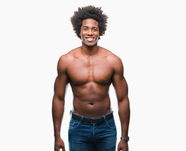 Hombre afroamericano sin camisa mostrando el cuerpo desnudo sobre un fondo aislado con una sonrisa feliz y fresca en la cara. Persona afortunada
. - Foto, imagen