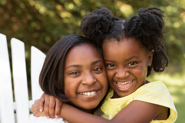 Portrait of two African American sisters hugging outside. - Foto, imagen