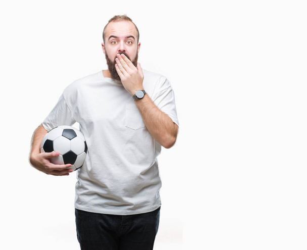Νέοι Καυκάσιος hipster άνδρα να κρατάει την μπάλα ποδοσφαίρου ποδοσφαίρου πάνω από το στόμα κάλυμμα απομονωθεί φόντο με το χέρι σοκαρισμένος με ντροπή για λάθος, έκφραση του φόβου, φοβάται στη σιωπή, μυστική έννοια - Φωτογραφία, εικόνα