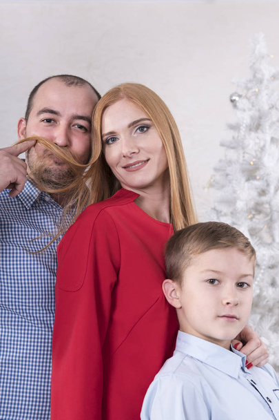 Humorous family portrait of a mother, father and son near a Christmas tree - Fotografie, Obrázek