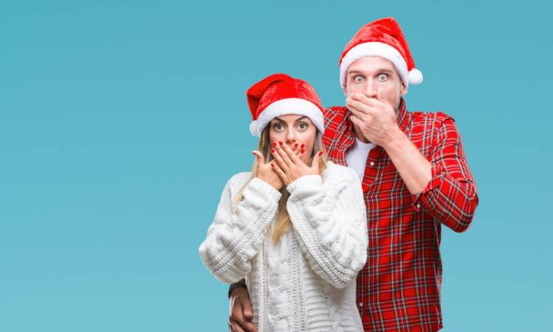Giovane coppia innamorata indossa cappello di Natale su sfondo isolato scioccato copertura bocca con le mani per errore. Concetto segreto
. - Foto, immagini