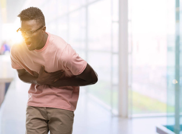 Молодий афроамериканець людиною носіння рожева маєчка з боку на живіт, тому що нудота, хворобливе захворювання самопочуття. Ache концепції. - Фото, зображення