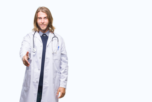 Young handsome doctor man with long hair over isolated background smiling friendly offering handshake as greeting and welcoming. Successful business. - Photo, Image