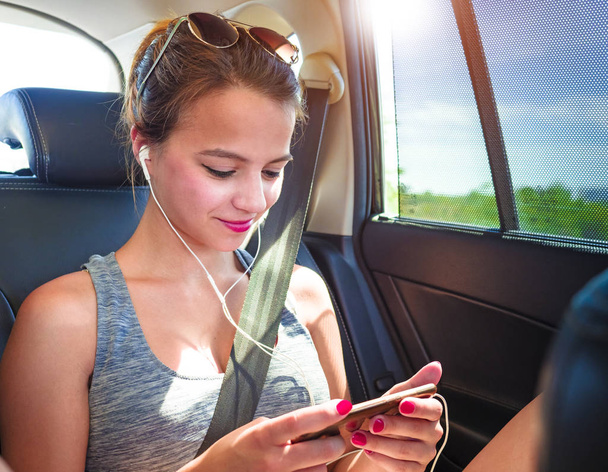 A happy teenage girl looking at the ecre of his smartphone while sitting in a van wearing headphones. - Zdjęcie, obraz