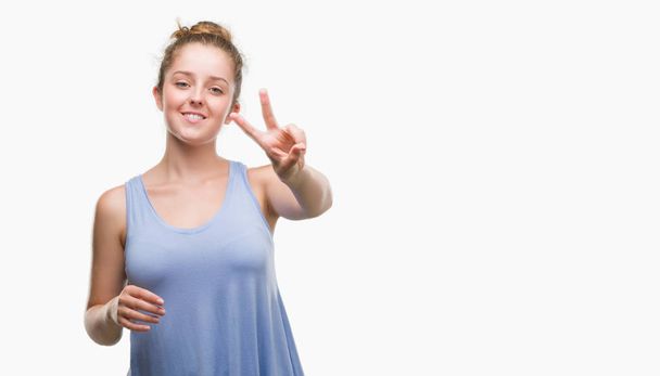 Young blonde woman smiling looking to the camera showing fingers doing victory sign. Number two. - Photo, Image