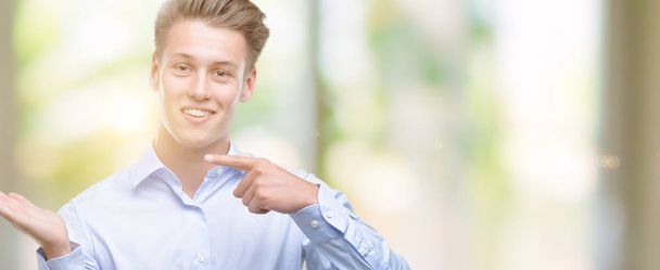 Jeune homme blond beau très heureux pointant avec la main et le doigt
 - Photo, image