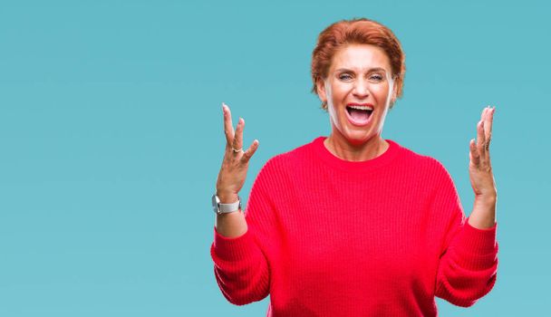 Atrractive senior caucasian redhead woman wearing winter sweater over isolated background celebrating mad and crazy for success with arms raised and closed eyes screaming excited. Winner concept - Foto, afbeelding