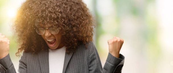 Афро-американських бізнес жінка в окулярах дуже щасливий і схвильований робить переможець жест з Вдивіться, посміхаючись і кричав на успіх. Святкування концепції. - Фото, зображення