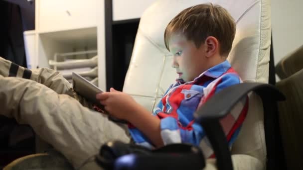 Happy young boy playing on his tablet sitting on the chair at home. - Footage, Video