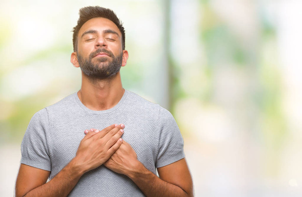 Adult hispanic man over isolated background smiling with hands on chest with closed eyes and grateful gesture on face. Health concept. - Foto, Imagem