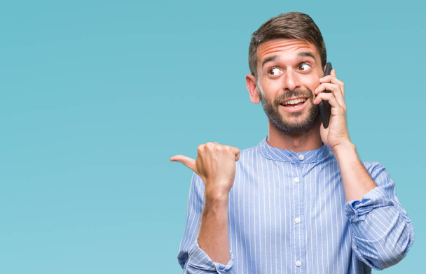 Young handsome man speaking on the phone over isolated background pointing and showing with thumb up to the side with happy face smiling - Foto, Imagem
