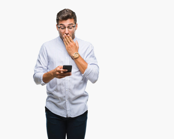 Young handsome man texting using smartphone over isolated background cover mouth with hand shocked with shame for mistake, expression of fear, scared in silence, secret concept - 写真・画像