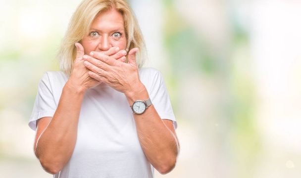 Femme blonde du moyen âge sur fond isolé choqué couvrant la bouche avec les mains pour erreur. Concept secret
. - Photo, image