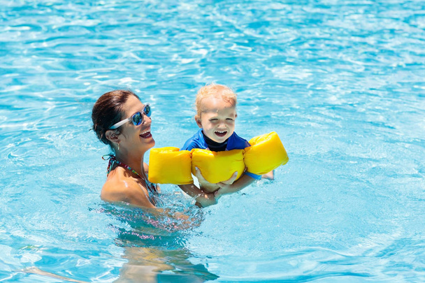 Matka i dziecko w odkrytym basenie tropikalnego ośrodka. Dzieciak uczy się pływać. Mama i dziecko bawią się w wodzie. Rodzinne letnie wakacje w egzotycznym miejscu. Aktywny i zdrowy sport dla dzieci. - Zdjęcie, obraz
