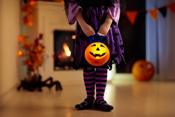 Boszorkány jelmez Halloween fogás vagy élvezet otthon a kislány. Sütőtök és gyertya dekoráció kandalló. Gyermek fogás vagy kezelő öltözött. Gyerek gazdaság candy vödör. Gyerekek ünneplik Halloween. - Fotó, kép