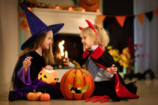 Dziewczynka w stroju czarownicy i chłopiec przebrany za wampira na Halloween trick lub psikus. Dzieci cukierek lub psikus z wiadrem cukierków. Dzieci świętują Halloween w kominku z dyni i latarni. - Zdjęcie, obraz
