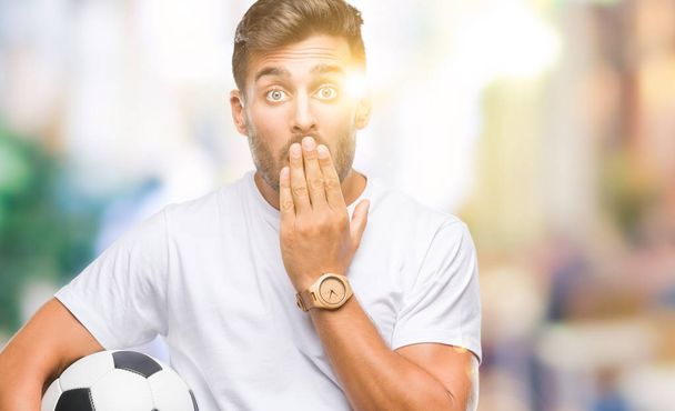 Mladý pohledný muž drží míč fotbal fotbal izolované pozadí kryt ústa rukou v šoku se studem za chybu, výraz strachu, strach v tichosti, tajné koncept - Fotografie, Obrázek