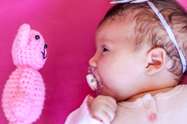 Grappig beeld van een Kaukasische pasgeboren baby babymeisje kijkend naar de teddybeer van aangezicht tot aangezicht. Ontdek het nieuwe concept van de wereld, nieuwe dingen te leren. Een maand oud kind. - Foto, afbeelding