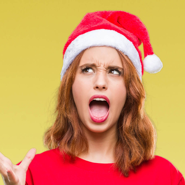 狂気と叫ぶと積極的な表現と腕を上げると叫んで怒ってクリスマス帽子をかぶっている孤立した背景に若くてきれいな女性。欲求不満のコンセプト. - 写真・画像