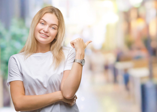 Young caucasian woman over isolated background smiling with happy face looking and pointing to the side with thumb up. - Photo, Image