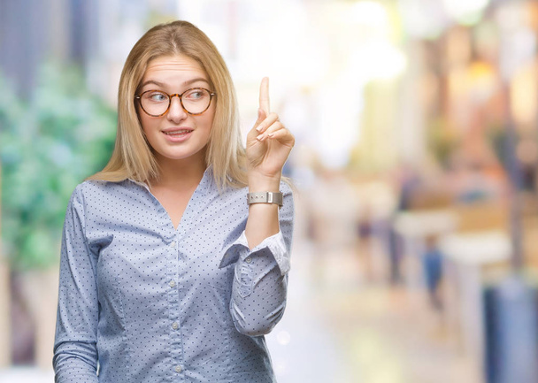 Giovane donna d'affari caucasica indossa occhiali su sfondo isolato puntando il dito verso l'alto con l'idea di successo. Uscito e felice. Numero uno.
. - Foto, immagini