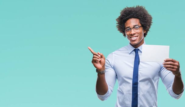 Afro american man holding blank card over isolated background very happy pointing with hand and finger to the side - Fotoğraf, Görsel