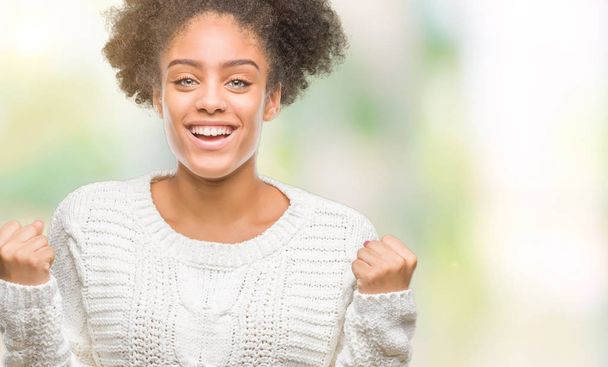 Nuori afro amerikkalainen nainen yllään talvi villapaita yli eristetty tausta juhlii yllättynyt ja hämmästynyt menestystä kädet kohotettu ja avoimet silmät. Voittajan käsite
. - Valokuva, kuva