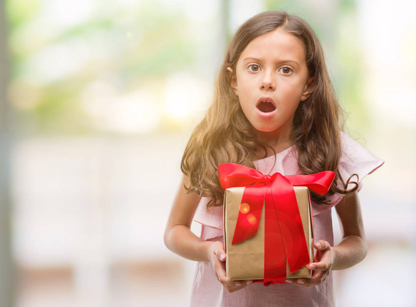Brunette-Spaanse meisje houdt een geschenk bang in schok met een verrassing gezicht, bang en opgewonden met angst expressie - Foto, afbeelding