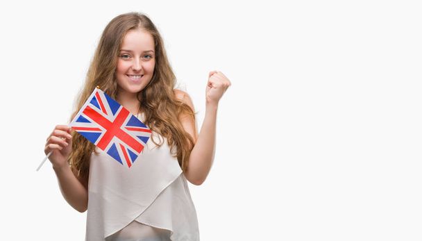 Młoda Blondynka kobieta trzyma flagę Wielkiej Brytanii krzyczy dumny i świętuje zwycięstwo i sukces bardzo podekscytowany, doping emocji - Zdjęcie, obraz