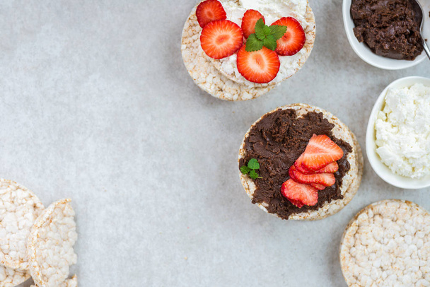 Healthy Snack from Rice Cakes with Ingredients nearby such as Ricotta Cheese, Chocolate Nut Spread and Strawberries on Light Background - Photo, Image
