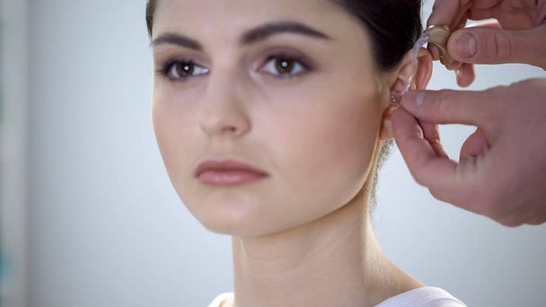 Physician putting deaf aid on young womans ear, hearing impairment treatment - 写真・画像