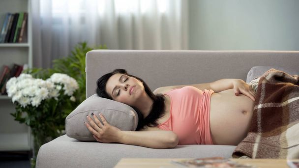 Relaxed pregnant lady sweetly sleeping on sofa, hugging her tummy with baby - Foto, Imagen