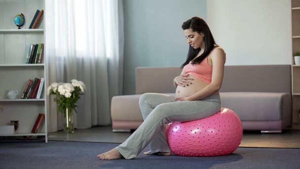 Joven embarazada escuchando a sus bebés golpeando, sentado en la pelota de fitness
 - Foto, imagen