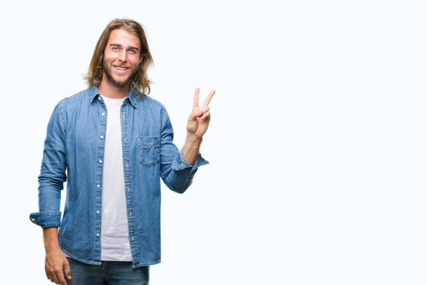 Young handsome man with long hair over isolated background smiling with happy face winking at the camera doing victory sign. Number two. - Photo, Image