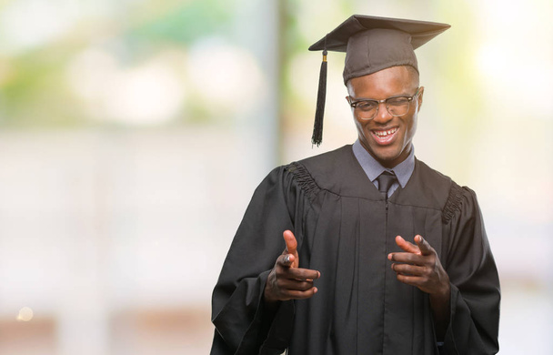 Young graduated african american man over isolated background pointing fingers to camera with happy and funny face. Good energy and vibes. - Foto, imagen