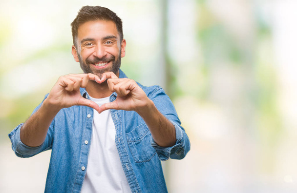 erwachsener hispanischer Mann mit isoliertem Hintergrund, der verliebt lächelt und Herzsymbol und Form mit Händen zeigt. Romantisches Konzept. - Foto, Bild